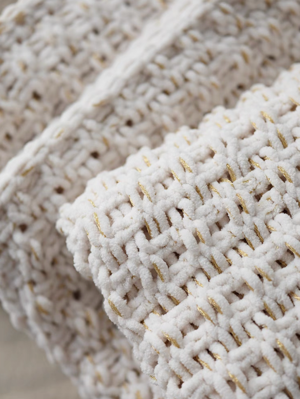 Close-up of folded white chunky knit throw blanket highlighting thick weave, soft texture, and gold thread accents