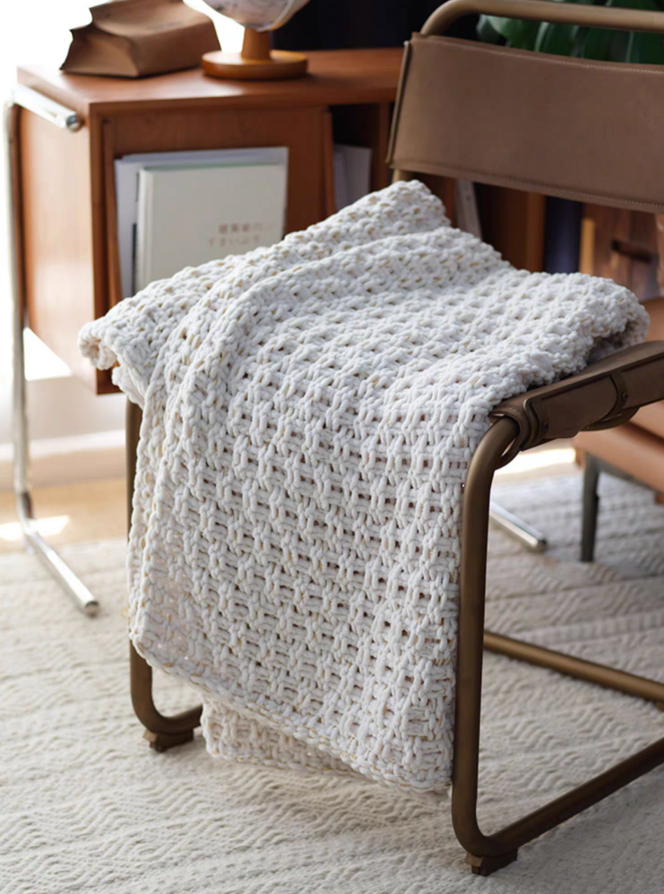 White chunky knit throw blanket neatly folded on chair seat in a warm modern interior