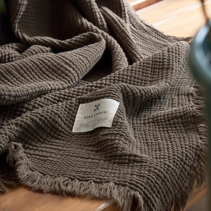 Grey green organic cotton waffle gauze throw blanket close-up showing breathable textured weave and fringe.