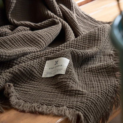 Grey green organic cotton waffle gauze throw blanket close-up showing breathable textured weave and fringe.