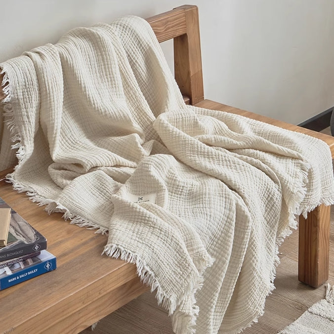 Ivory white waffle textured organic cotton fringe throw blanket draped over a wooden bench in a minimalist home interior.