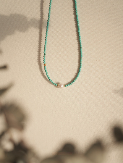 Close-up of micro turquoise bead choker with freshwater pearl on textured fabric background with warm lighting
