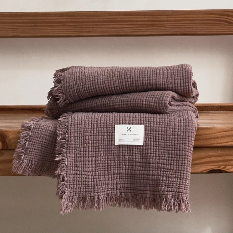 Mocha purple organic cotton waffle throw blanket folded neatly on wooden bench with soft fringe edges.