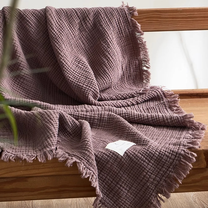Mocha purple waffle textured organic cotton fringe throw blanket draped over wooden chair in cozy home setting.