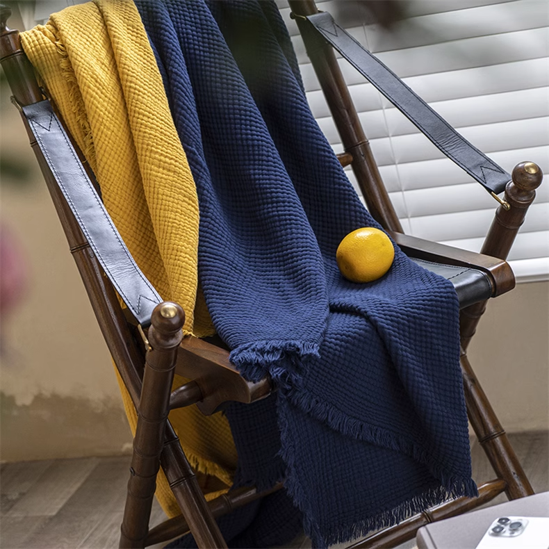 Navy blue and yellow organic cotton waffle textured throw blankets draped over wooden chair with soft fringe detailing.