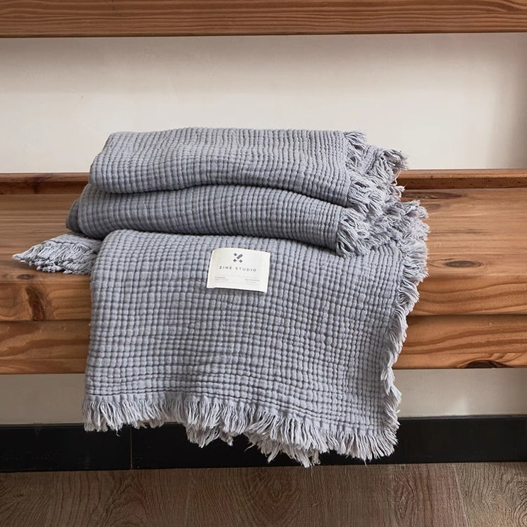 Smoky blue organic cotton waffle textured throw blanket folded neatly on wooden bench with fringe edges.