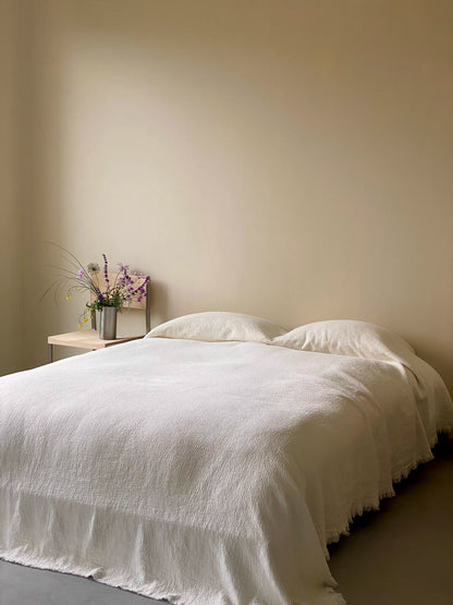 Stonewashed ivory white French flax linen duvet thin quilt draped across bed showing natural breathable linen bedding
