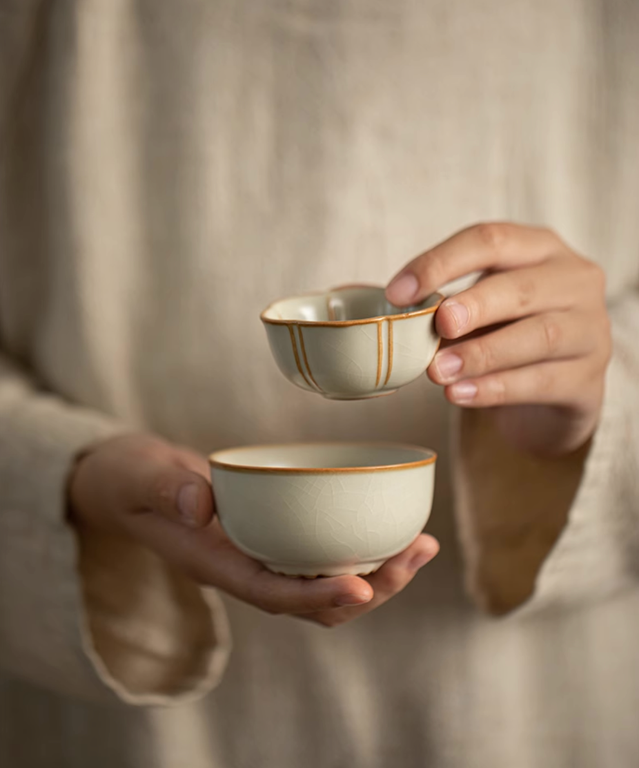 Light yellow Ru kiln ceramic tea cups stacked together and held in hands
