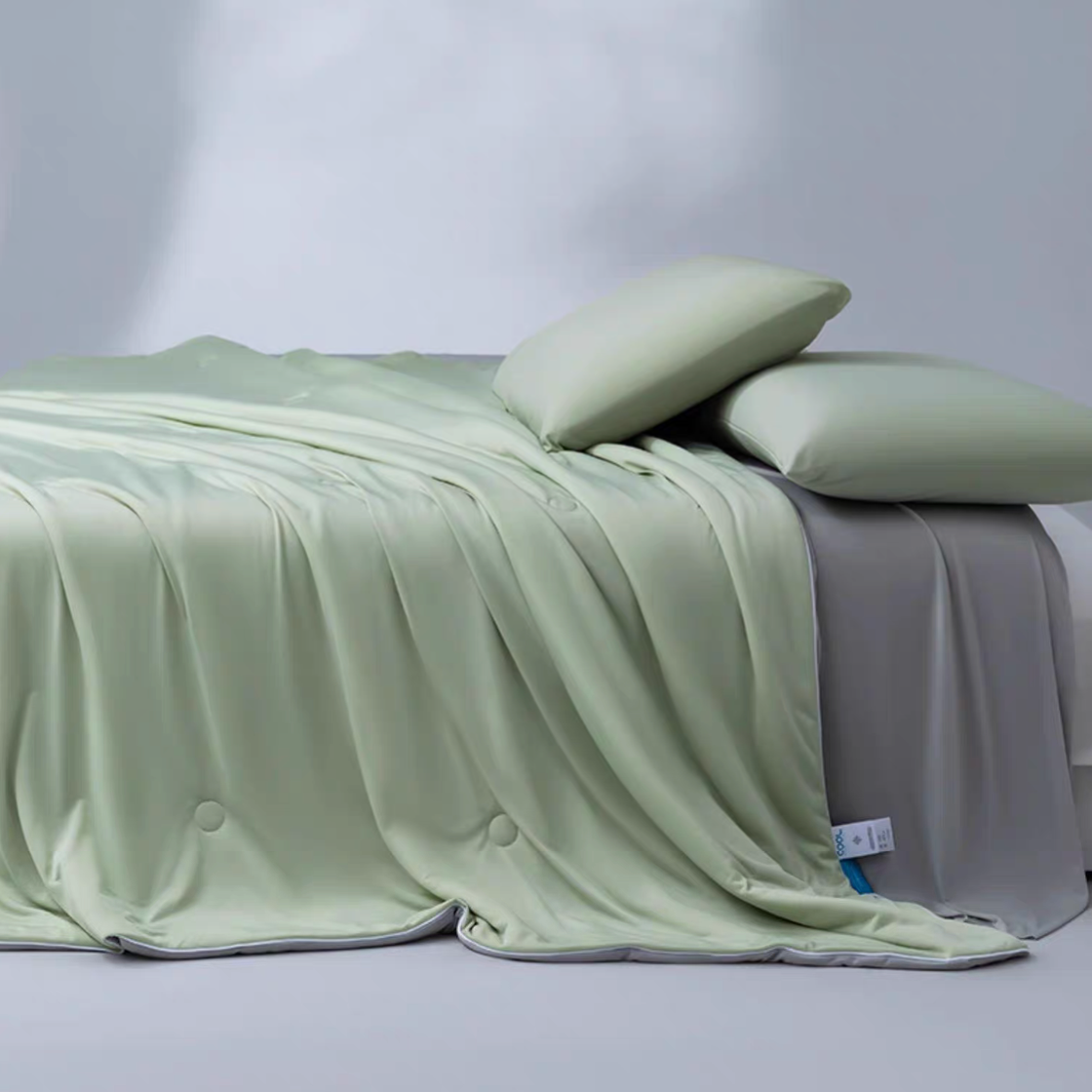 Green and gray cooling summer comforter layered across a bed with soft pillows, designed for breathable summer sleep.