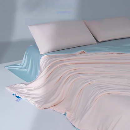 Pink and blue cooling summer quilt draped across a bed showing silky smooth lightweight cooling fiber fabric.