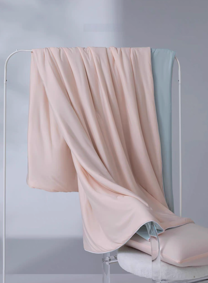 Pink and blue reversible cooling antibacterial summer quilt hanging on a rack with smooth moisture-wicking cooling fabric.