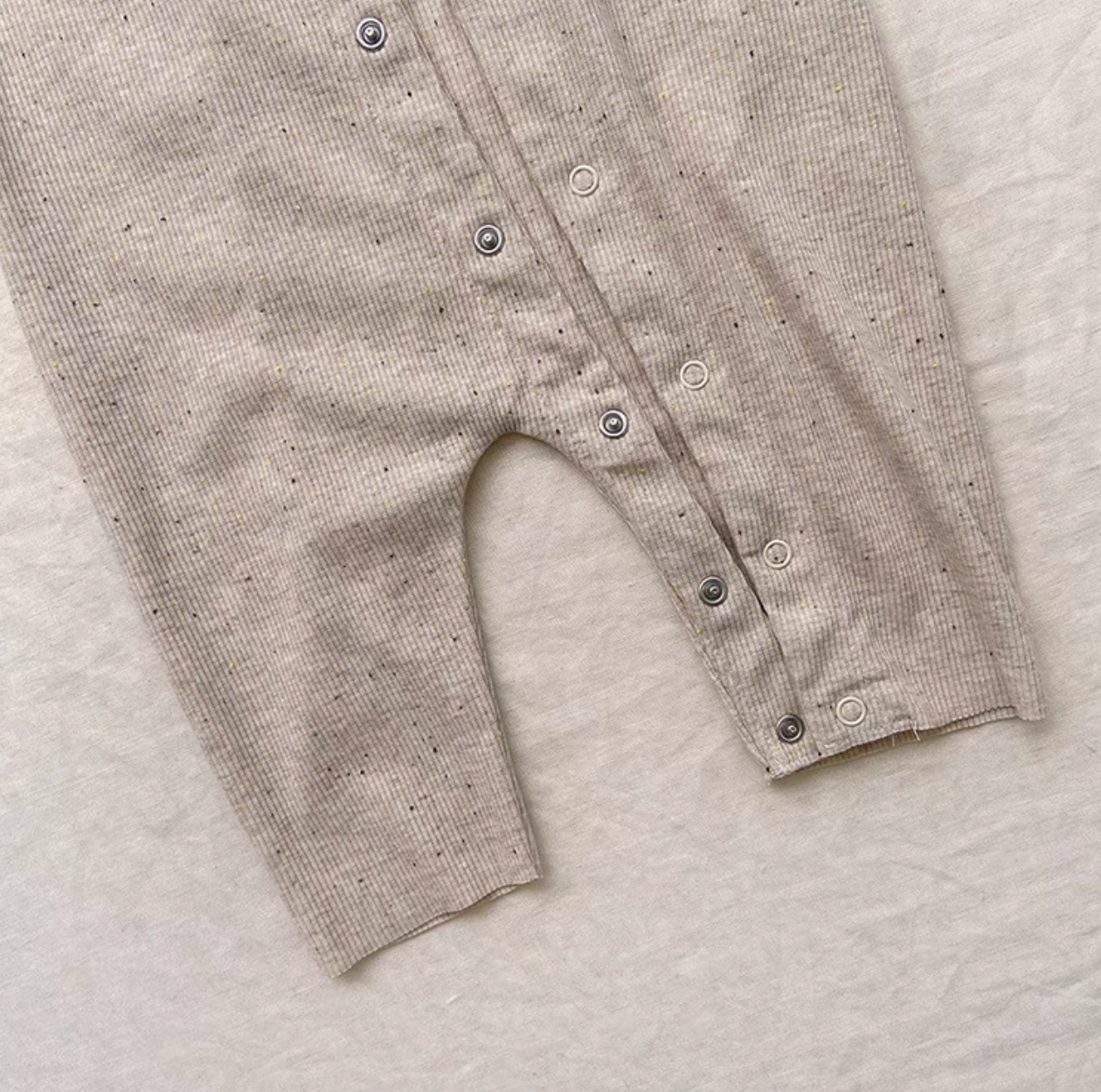 Close-up detail of oatmeal beige baby romper showing snap buttons and fabric texture
