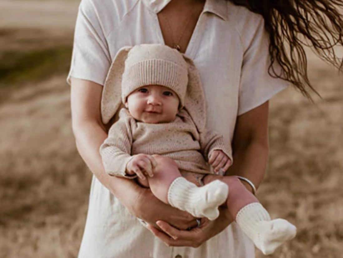 Baby wearing oatmeal beige romper set with bunny ear hat outdoor lifestyle photo