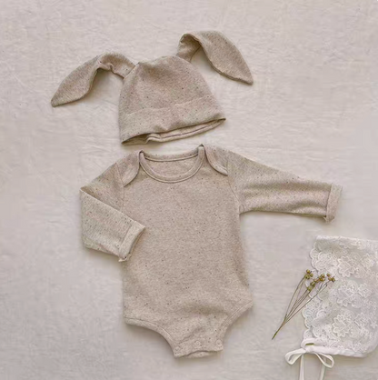 Flat lay oatmeal beige baby bodysuit with bunny ear hat showing soft cotton texture