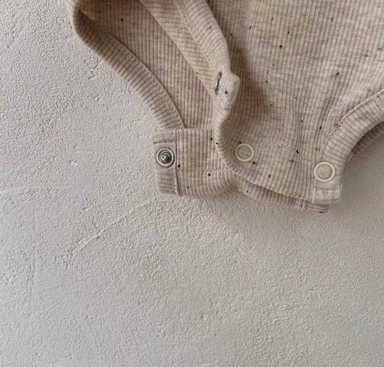 Close-up of snap button bottom on oatmeal beige baby romper for easy diaper change