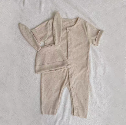 Oatmeal beige short sleeve long baby romper with bunny ear hat laid flat on fabric