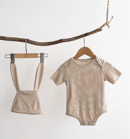 Oatmeal beige short sleeve baby bodysuit with bunny ear hat hanging on wooden rack
