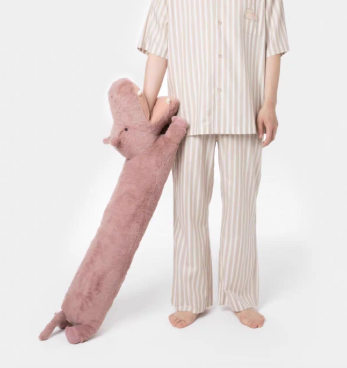 Pink hippo long body pillow standing upright next to person highlighting full length and cuddly design