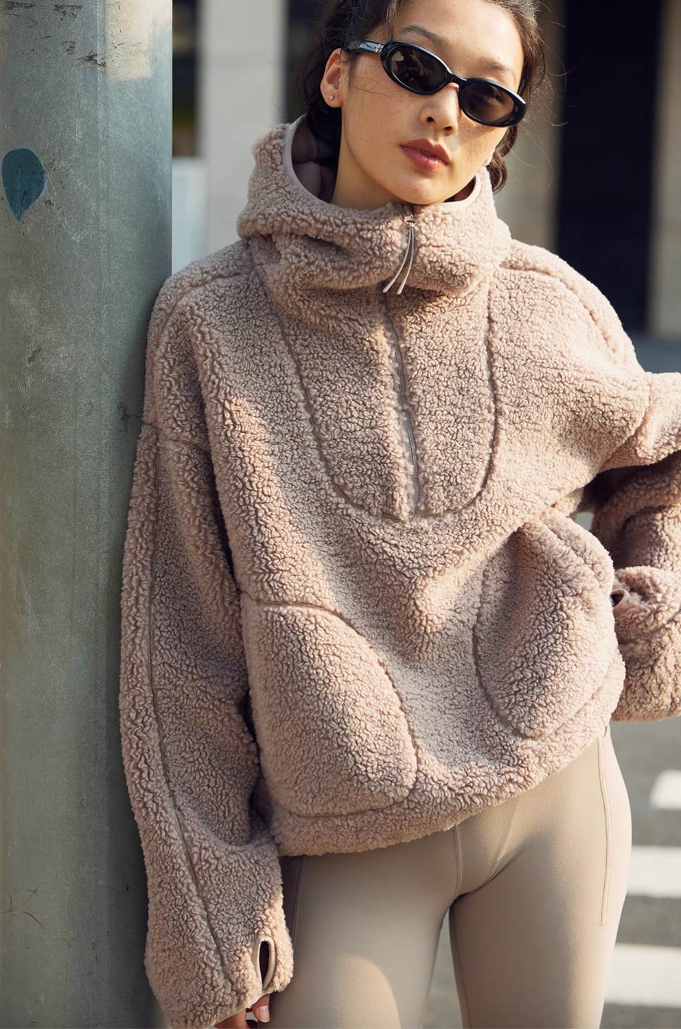 Model wearing Cozy Sherpa Thermal Hoodie Pullover in brown leaning outdoors, featuring half-zip closure, oversized fit, and plush sherpa texture