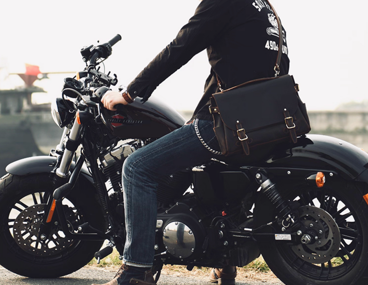 Man on motorcycle wearing brown crazy horse leather satchel across shoulder.