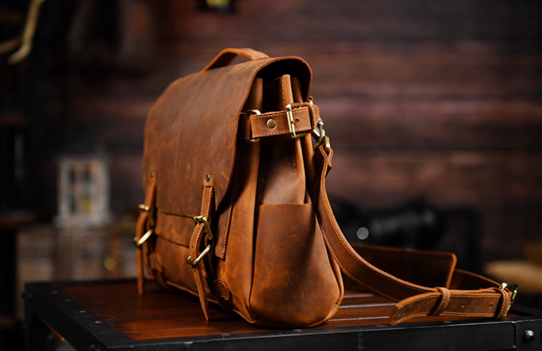 Side angle of brown leather satchel showing side pocket and adjustable strap buckle.