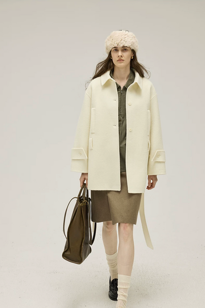 Cream double-face wool coat in motion, showing the point collar, welt pockets, and cuff tabs