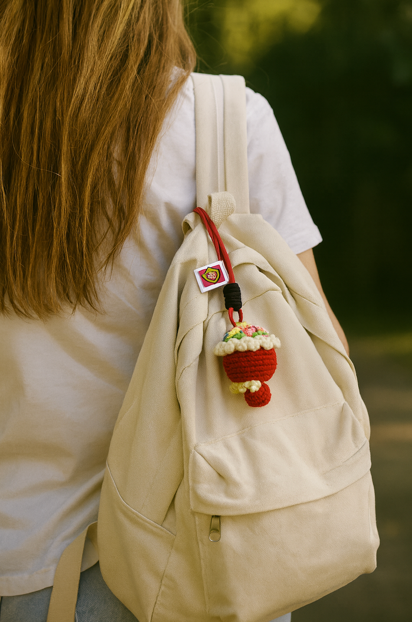 Handmade red crochet flower bouquet keychain with rope loop, hanging on a beige backpack outdoors.