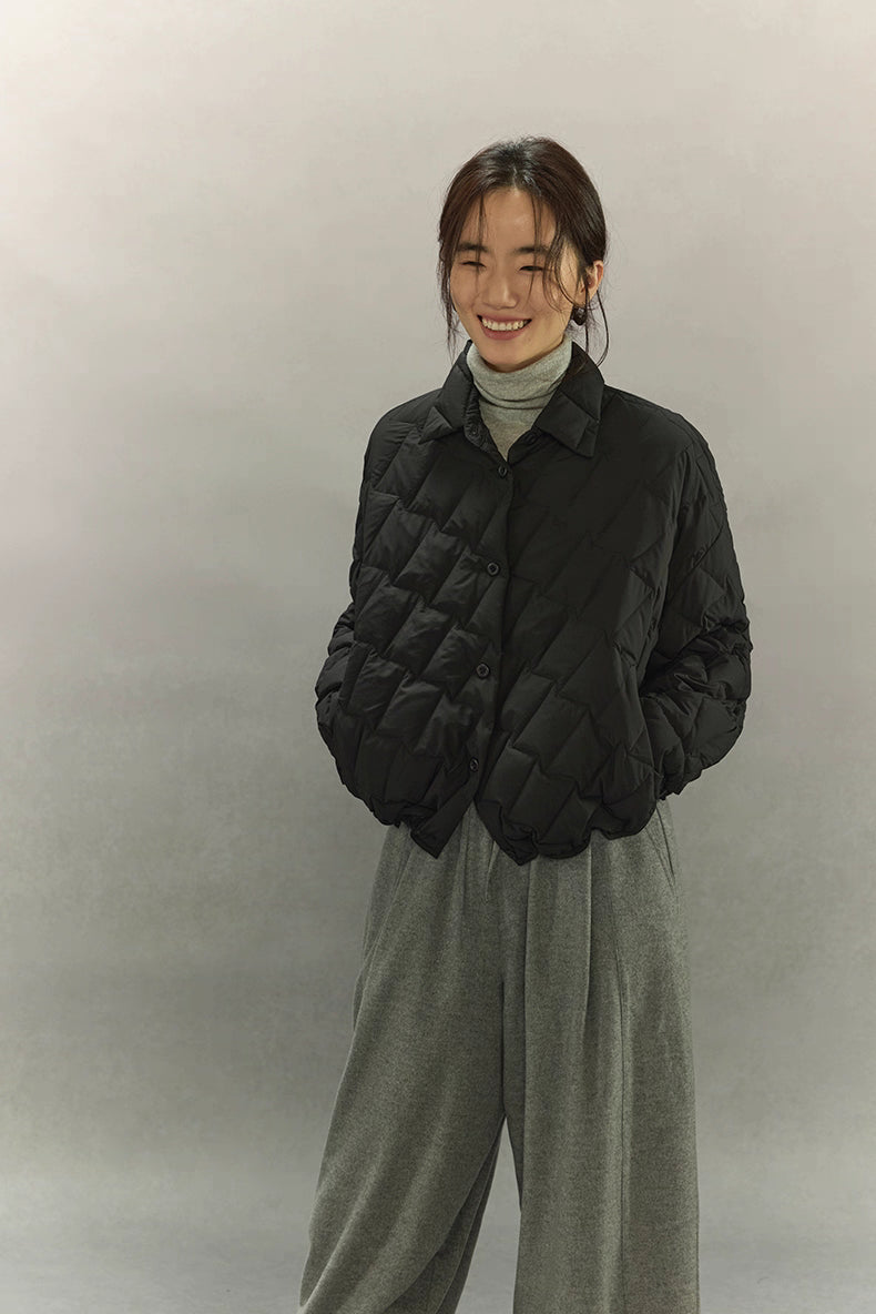 Woman smiling in black cropped quilted goose down shirt jacket, hands in pockets, minimalist studio background.