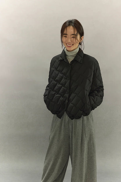 Woman smiling in black cropped quilted goose down shirt jacket, hands in pockets, minimalist studio background.