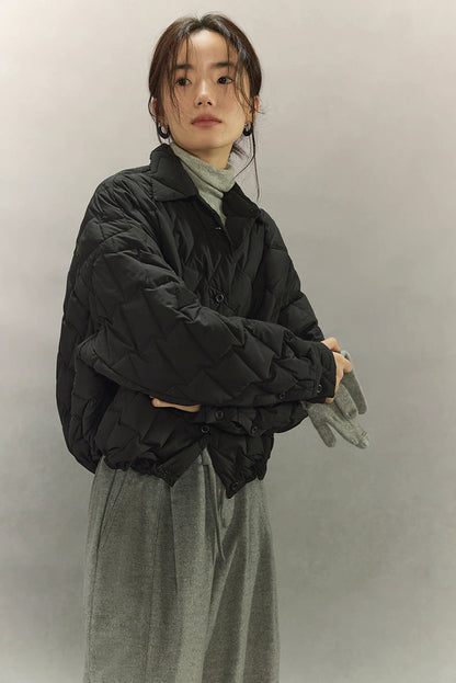 Close side view of black cropped quilted goose down shirt jacket styled with grey turtleneck and wide-leg trousers.