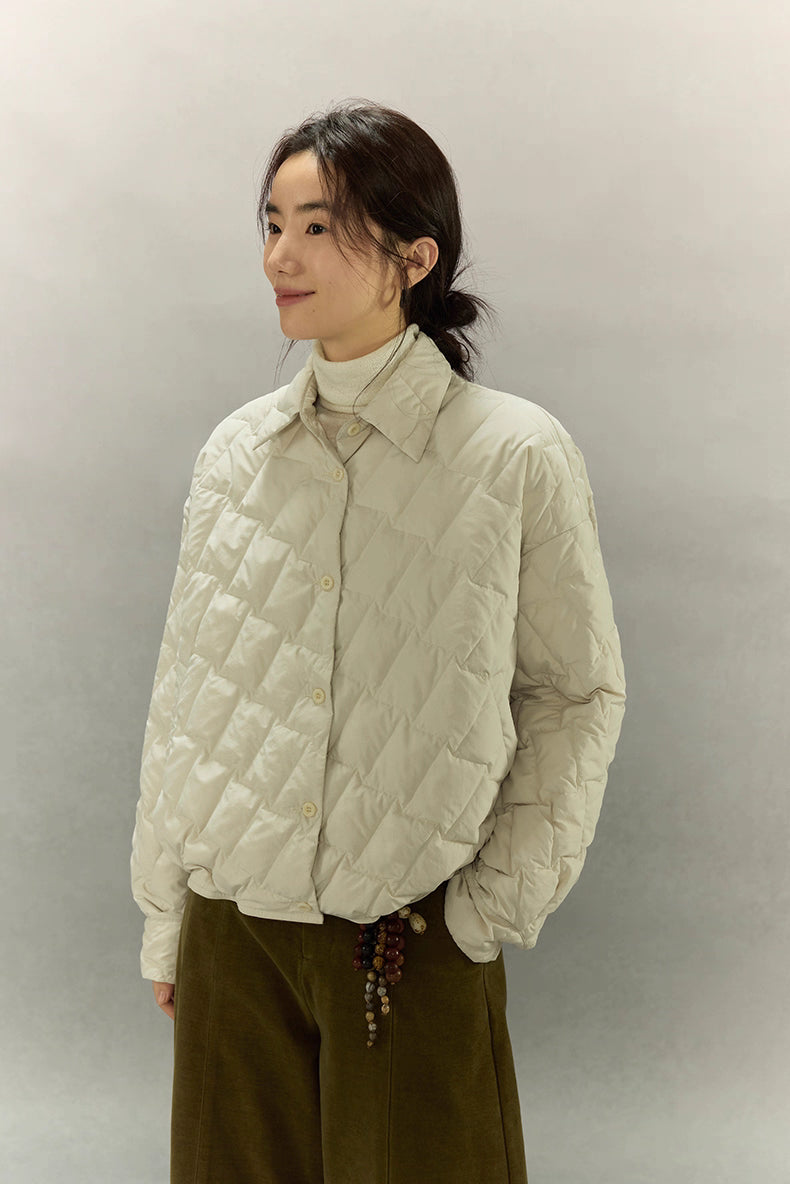 Close three-quarter side view of cream beige cropped quilted goose down shirt jacket layered over a turtleneck.