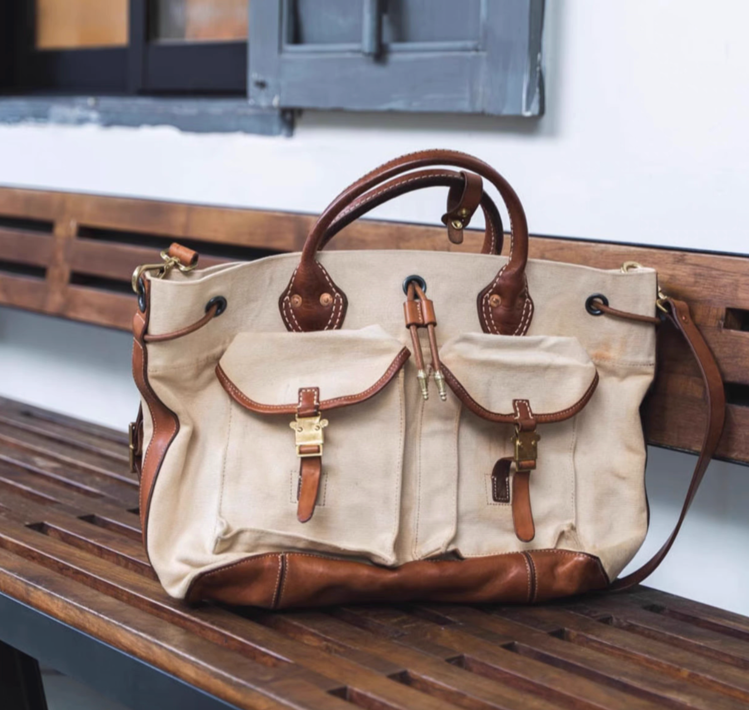 Beige canvas and brown leather weekender tote on wooden bench outdoors