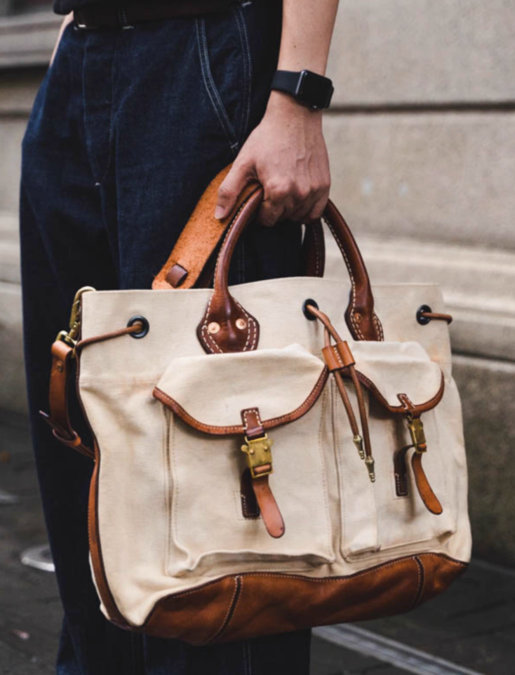 Man carrying handcrafted beige canvas and leather travel tote by handles