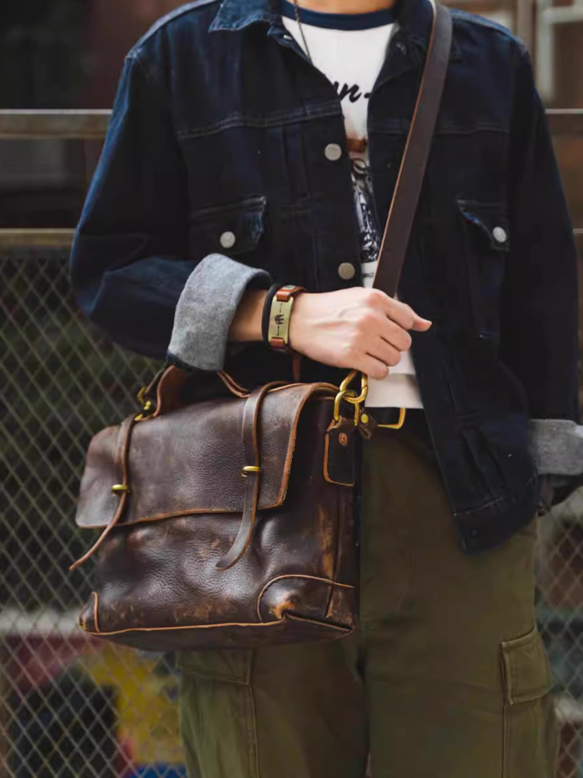 Person wearing denim jacket and carrying brown full-grain leather messenger bag crossbody style