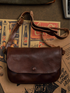 Dark brown full-grain leather crossbody bag laid flat on vintage paper backdrop with 7up posters