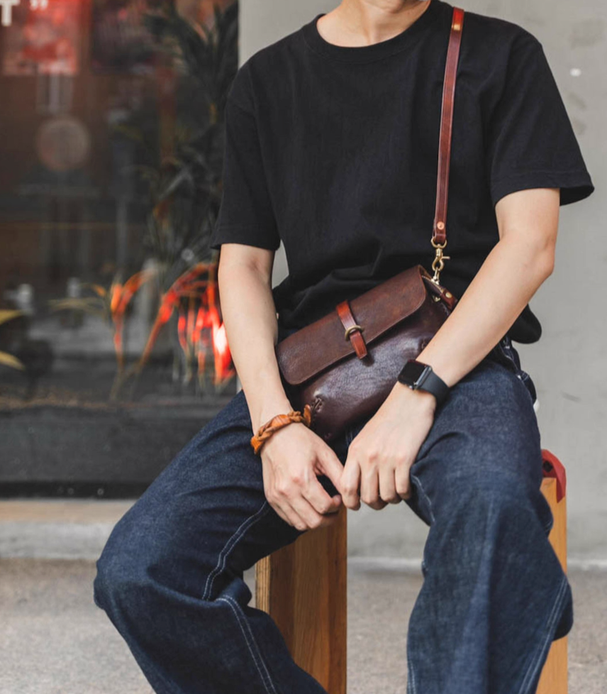 Man sitting with espresso brown Italian leather crossbody bag styled with jeans and black tee
