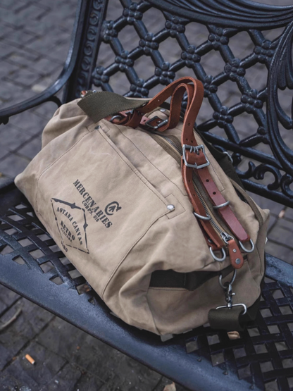 Retro waxed canvas duffel bag with leather straps resting on metal bench outdoors