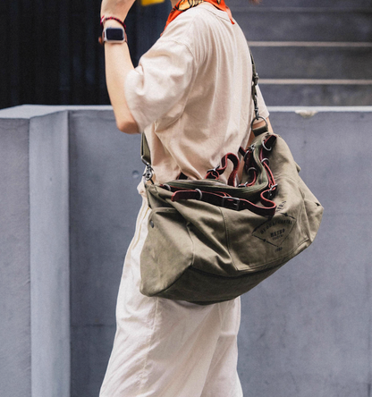 Model wearing green vintage canvas duffel bag over shoulder in casual outfit