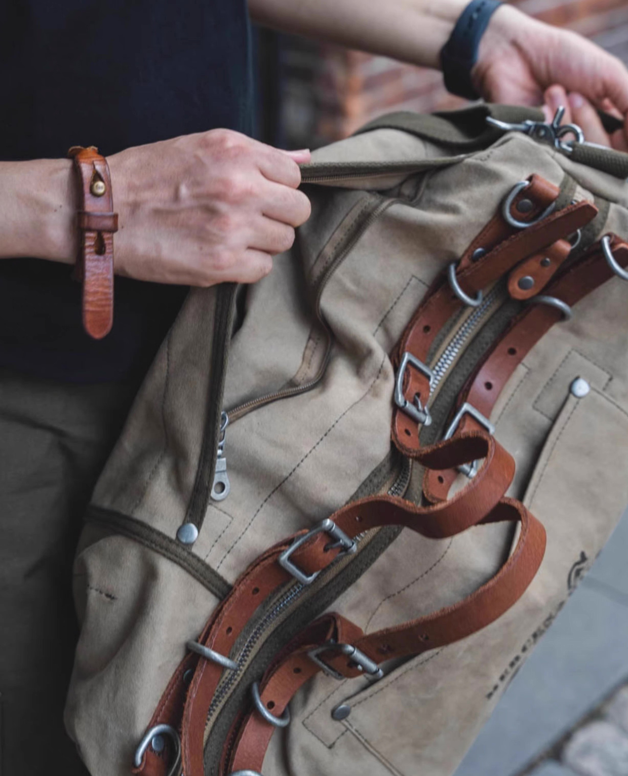 Person holding open vintage waxed canvas travel duffel with brown leather straps