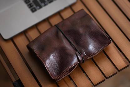 Folded dark brown leather refillable notebook beside a laptop on wooden slat desk, highlighting soft vintage texture.