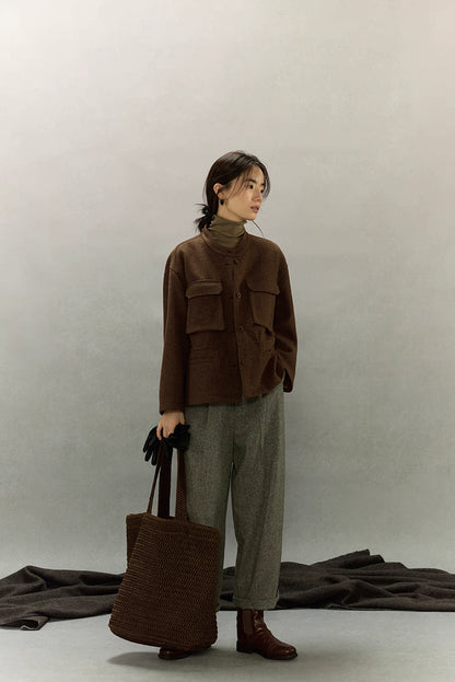 Full-length view of woman in dark coffee alpaca wool field jacket, grey pants, brown boots and knitted tote bag