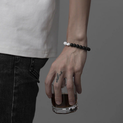 Cracked lava stone bracelet with black and white beads worn on wrist while holding glass highlighting minimalist contrast style