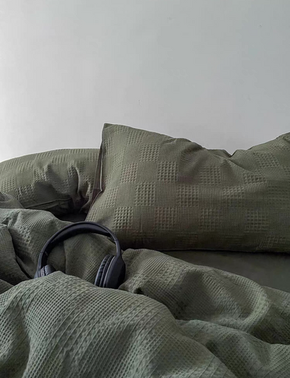 Army green waffle-weave duvet and oversized pillow; minimal bed scene with headphones for a relaxed aesthetic.