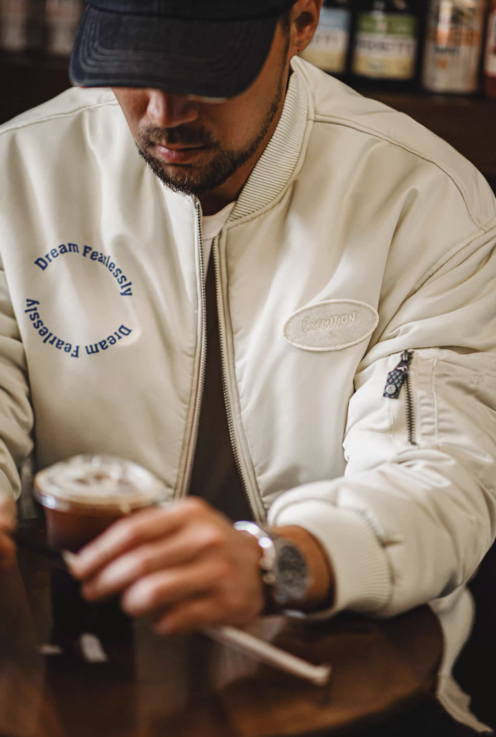 Model sitting at café wearing MA-1 bomber with iced coffee on table