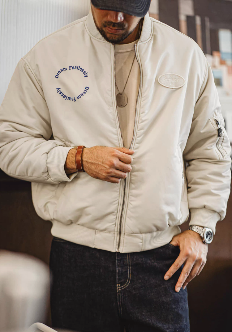 Man wearing almond MA-1 bomber indoors styled with jeans and leather bracelet
