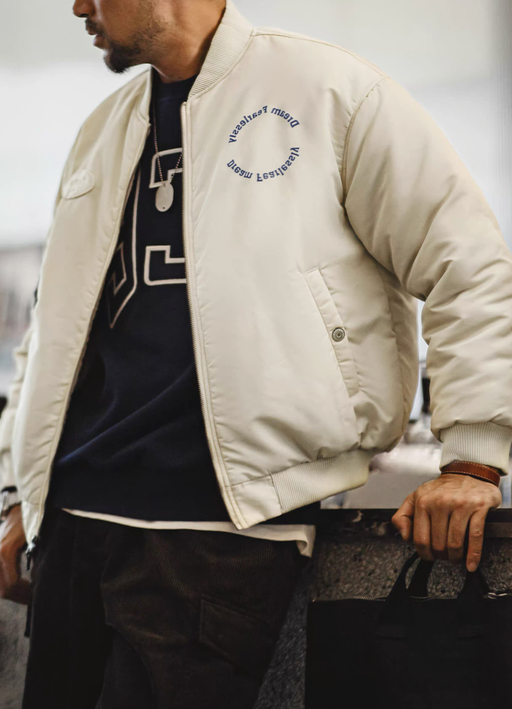 Model layering cream bomber over navy sweatshirt for casual streetwear look