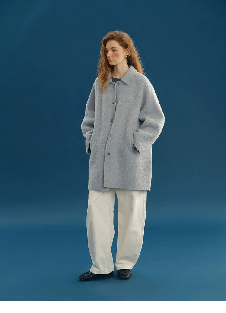 Full-length view of a Dusty Blue mid-length alpaca-wool coat buttoned with hands in pockets