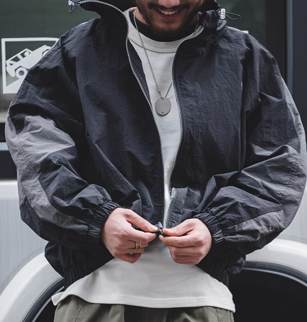Man wearing Sumatra Black Dynamic Layering Jacket adjusting zipper highlighting dual zip design and lightweight texture