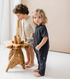 Toddler wearing charcoal gray cotton romper standing beside wooden table indoors
