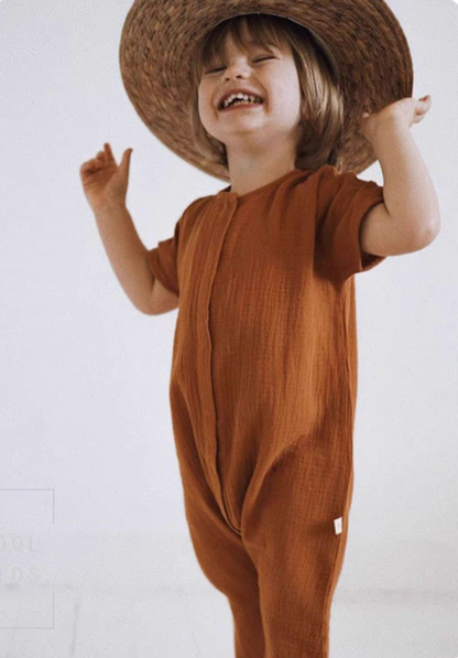Happy toddler wearing orange red cotton romper and straw hat smiling